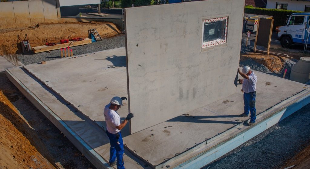 Zwei Mitarbeiter platzieren eine Wand während eines Kellerbaus.